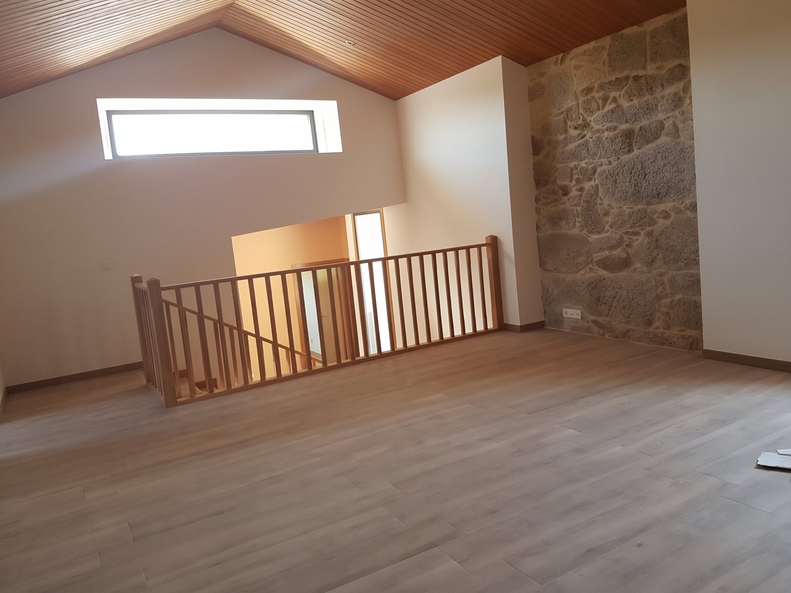 Espacio interior con entreplanta, muro de piedra vista y techo de madera con geometría en Y en vivienda rehabilitada en Tui