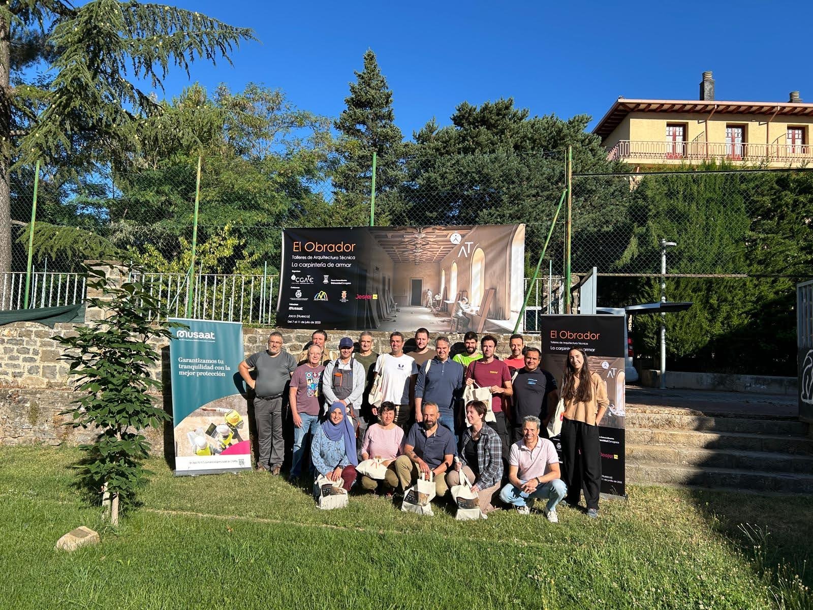 Grupo de participantes y profesores frente al cartel oficial de El Obrador: La carpintería de armar en Jaca del 7 al 11 de julio de 2025
