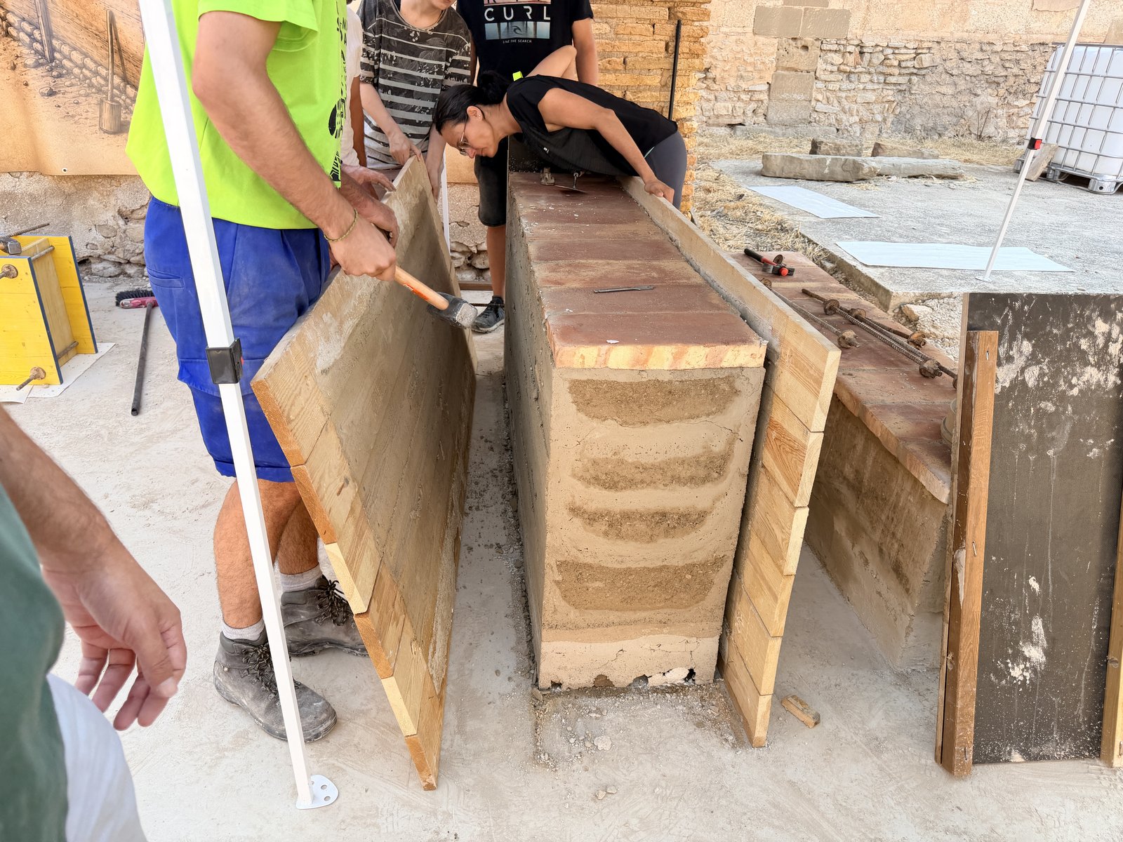 Proceso de desencofrado de los tableros de madera (tapialera) de un muro experimental de tapial calicostrado con coronación de ladrillo macizo