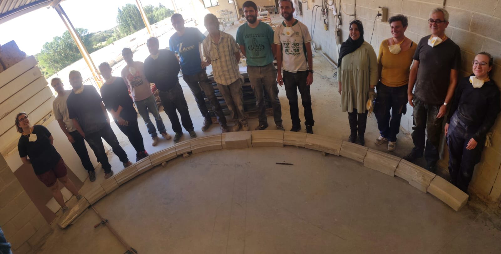 Asistentes y profesores del curso El Obrador: trazas de montea y cortes de cantería en Uncastillo junto al arco completo de dovelas de piedra