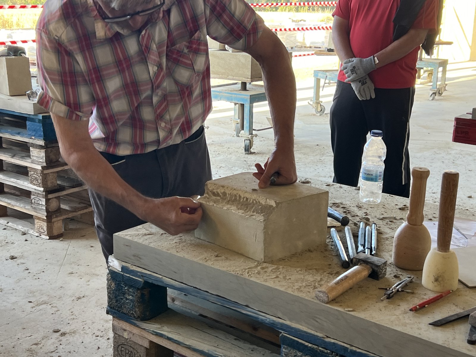 El maestro cantero Pedro Anía Pérez realizando el desbaste de aristas y planos de referencia en un bloque de piedra arenisca con maceta y cincel