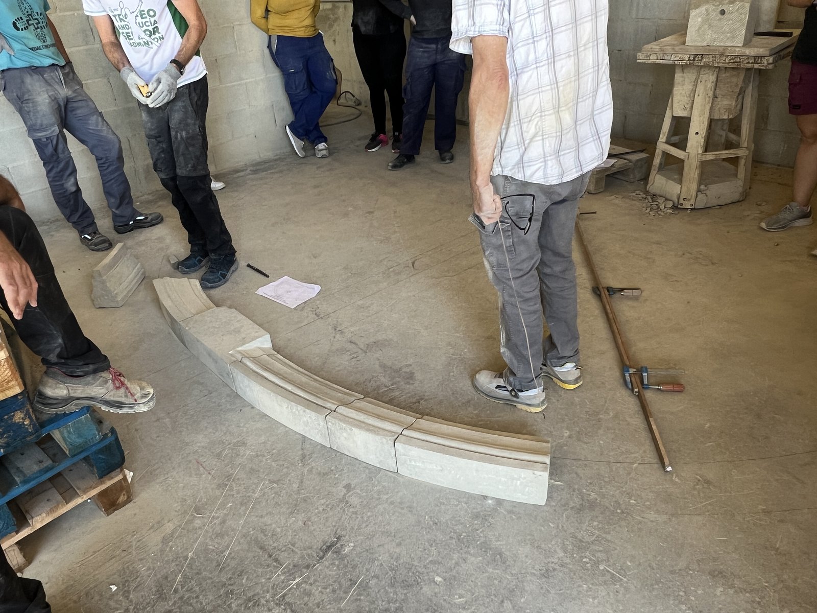 Dovelas de piedra y clave presentadas sobre el arco trazado en el suelo del taller junto al compás de vara de madera